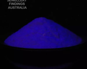 May include: A close-up of a pile of bright blue glow-in-the-dark powder in a black bowl. The powder is very fine and has a slightly sparkly appearance.