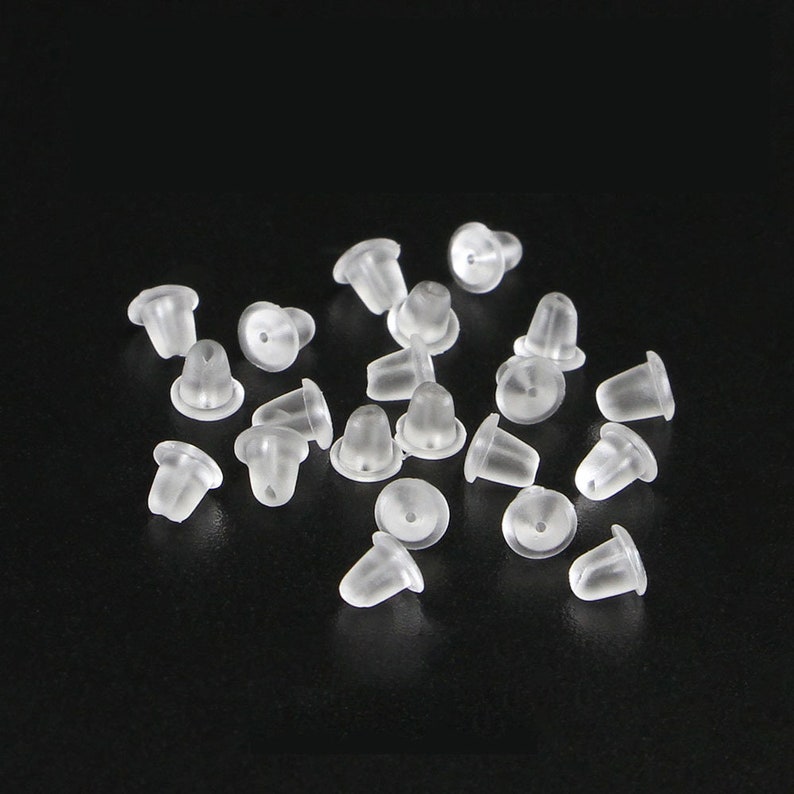 May include: A selection of clear, translucent earring backs, set against a black backdrop. The earring backs are small, with a conical form and a flat, circular base. They appear to be made of soft plastic or silicone.