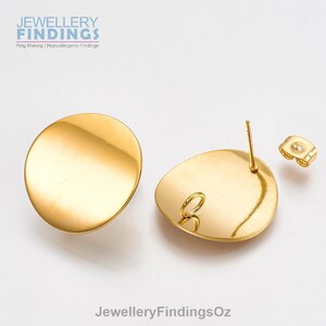 May include: A pair of gold-toned round earring blanks with a smooth, slightly domed surface. The earring blanks have a post and a butterfly back.