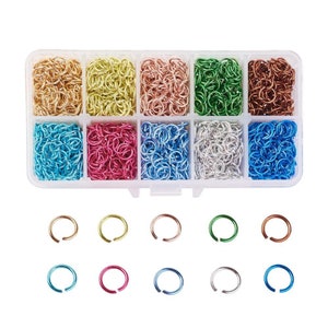May include: A clear plastic organiser filled with various coloured jump rings. The colours include gold, yellow, rose gold, green, copper, turquoise, pink, blue, silver, and dark blue. Additional jump rings of various colours are displayed below.