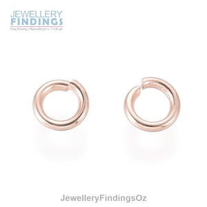 Könnte beinhalten: Zwei roségoldene Sprungringe, jeder mit einem Durchmesser von etwa 6 mm. Diese Ringe sind ideal für die Schmuckherstellung und das Basteln.