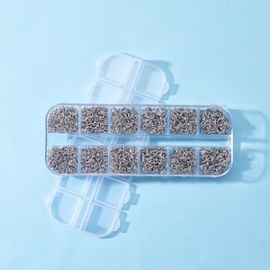May include: A clear plastic storage box with 12 compartments filled with small silver jump rings. The box is open and the compartments are visible.