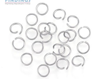 May include: A close-up of a pile of silver jump rings. The rings are all the same size and are arranged in a random pattern. The rings are used for jewelry making.