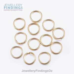 Könnte beinhalten: Nahaufnahme von 12 goldenen Sprungringen, kleinen Metallringen, die in der Schmuckherstellung verwendet werden. Die Ringe sind auf einem weißen Hintergrund verstreut angeordnet.