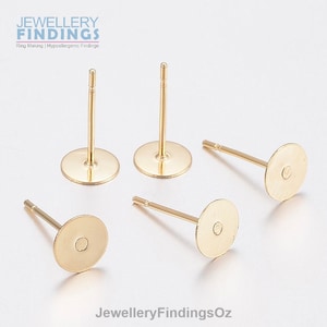 Op de afbeelding: Vier gouden oorringblanks met ronde pads en pinnen. De oorringblanks liggen op een wit oppervlak. JewelleryFindingsOz.