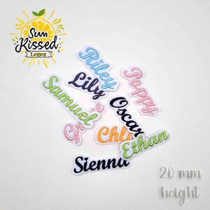 Op de afbeelding: Een verzameling geborduurde naamlabels in diverse kleuren, waaronder lichtblauw, donkerpaars, limoengroen, roze, oranje en zwart. Elk label heeft een cursief lettertype en een witte rand. De tekst 20 mm height is zichtbaar.