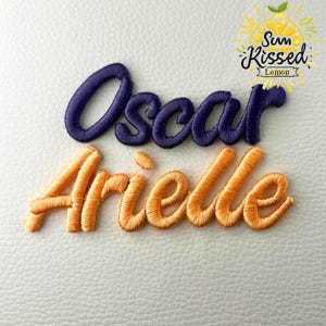 May include: Embroidered names "Oscar" in dark blue and "Arielle" in orange thread on a white textured surface. A "Sun Kissed Lemon" logo is in the upper right corner, featuring a lemon and sun design.