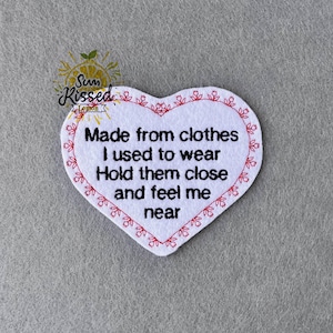 Könnte beinhalten: Ein weißes herzförmiges Patch mit rotem Blumensaum und dem Text: "Made from clothes I used to wear Hold them close and feel me near." Das Patch hat ein Logo in der oberen linken Ecke mit der Aufschrift "Sun Kissed Lemon".