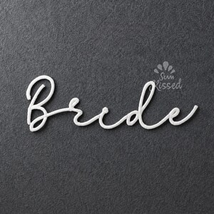 Puede incluir: Un recorte de palabra en escritura blanca que dice Bride en una fuente cursiva. Las letras presentan una textura suave y redondeada y están colocadas sobre un fondo gris oscuro texturizado. Un pequeño logotipo con el texto Sun Kissed es visible arriba.