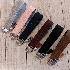 May include: Seven keychains with leopard print fabric and silver key rings. Each keychain has a tassel. The keychains are in various colors, including brown, black, pink, and gray.