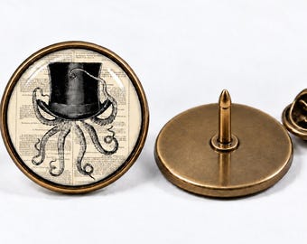Könnte beinhalten: Eine runde Anstecknadel mit einer schwarz-weißen Illustration eines Oktopus mit Zylinder vor einem Hintergrund aus antikem Wörterbuchtext. Die Nadel hat einen bronzefarbenen Metallrahmen und einen passenden bronzefarbenen Verschluss.