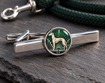 Könnte beinhalten: Eine silberfarbene Krawattenklammer mit einem runden Emblem, das eine cremefarbene Windhund-Silhouette vor einem dunkelgrünen Hintergrund mit geometrischen Strahlenlinien und schwarzen Akzenten zeigt, horizontal auf einer strukturierten Oberfläche.