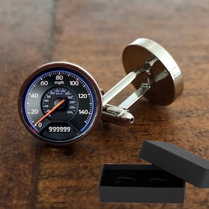 May include: Silver cufflinks with a black and blue speedometer design. The speedometer has a red needle pointing to 999999 and the text "mph" and "km/h".
