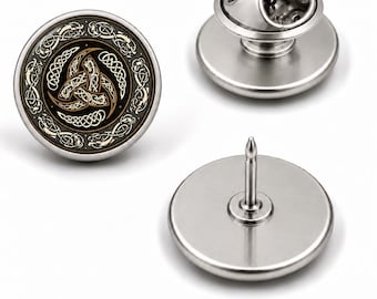 Könnte beinhalten: Eine runde Anstecknadel mit schwarzer Mitte und goldenem Triquetra-Knotenmuster, umgeben von einem silberfarbenen Rand mit komplexen Flechtmustern. Das Set zeigt die Vorderansicht, eine Seitenansicht mit Verschluss und die Rückseite.