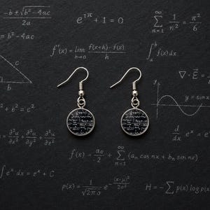May include: Silver-toned dangle earrings with circular pendants featuring mathematical formulas. The earrings hang against a dark background covered in equations and diagrams, creating a scholarly aesthetic. A unique accessory for science enthusiasts.