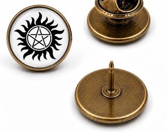Könnte beinhalten: Ein Set aus runden Anstecknadeln mit antikem Bronze-Finish. Eine Nadel zeigt ein schwarzes Pentagramm-Symbol, umgeben von stilisierten Flammen auf weißem Grund. Zwei weitere Nadeln zeigen die schlichte Bronzerückseite mit Metallstift und Verschluss.