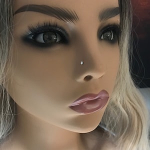 Könnte beinhalten: Nahaufnahme eines Gesichts mit einem kleinen, klaren Nasenring-Stecker. Die Person hat blondes Haar und trägt Make-up.