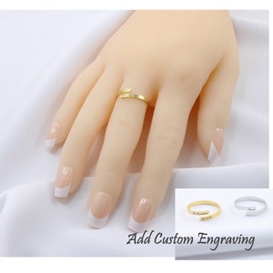 May include: Gold and silver wrap-around rings with the option to add custom engraving. The rings are shown on a model's finger.