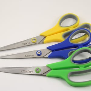 May include: Three pairs of personalised scissors with yellow, blue and green handles. The scissors are labelled "Chris", "Karen" and "Christy".