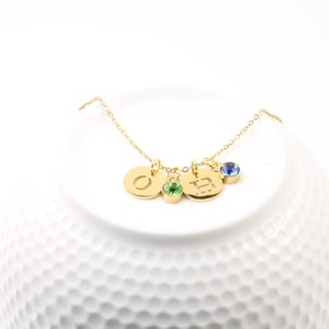 May include: A gold necklace with three charms, each featuring a letter and a small gemstone. The charms are a gold 'O' with a green gemstone, a gold 'H' with a blue gemstone, and a gold 'E' with a green gemstone.