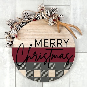 May include: A round wooden sign with a red and black plaid design. The sign says "Merry Christmas" in black lettering.