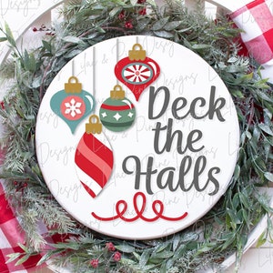 以下が含まれることがあります： 白い丸い木製の看板に、グレーの文字で「Deck the Halls」と書かれています。看板は、上からぶら下がっているカラフルなクリスマスオーナメント4つで飾られています。看板は緑のリースで囲まれています。