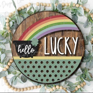 Könnte beinhalten: Ein rundes Holzschild mit einem Regenbogen, einem Topf mit einem Kleeblatt und den Worten "hello lucky". Das Schild hat einen grünen Hintergrund mit weißen Punkten.