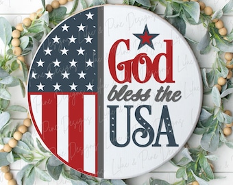 May include: A round wooden sign with a red, white, and blue American flag on the left side and the text "God bless the USA" in red and blue on the right side. The sign is surrounded by a wreath of green leaves and beige beads.
