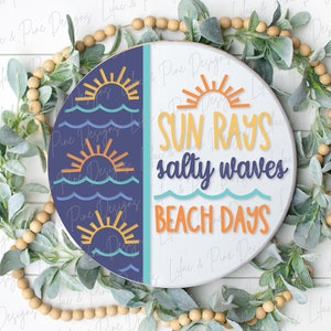 Op de afbeelding: Een rond houten bord met een blauwe en witte achtergrond. De linkerzijde heeft een patroon van oranje zonnen en blauwe golven. De rechterzijde heeft de tekst "SUN RAYS salty waves BEACH DAYS" in oranje, gele en blauwe letters.