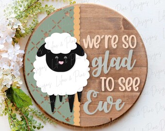 Könnte beinhalten: Ein rundes Holzschild mit grünem und pfirsichfarbenem Muster. Das Schild zeigt ein weißes Schaf mit schwarzen Augen und einer schwarzen Nase. Der Text "we're so glad to see Eve" ist in grauer und pfirsichfarbener Schrift geschrieben.