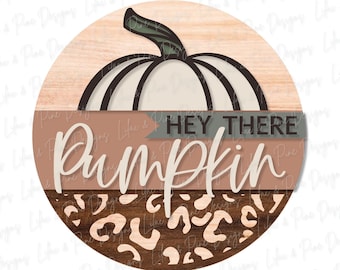 Könnte beinhalten: Ein rundes Holzschild mit einem braunen, weißen und grünen Kürbisdesign. Das Schild trägt die Aufschrift "Hey There Pumpkin" in rosa-weißer Schrift. Der untere Teil des Schildes hat ein braunes und weißes Leopardenmuster.
