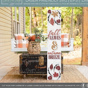 May include: A white wooden sign with the text "fall leaves & autumn breeze" in brown and gold lettering. The sign is decorated with red, orange, and brown leaves.