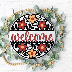 May include: A round wooden sign with a welcome message in red script. The sign is decorated with a black and white floral design with red and yellow flowers.