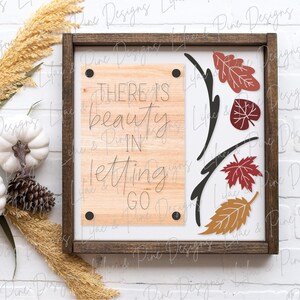May include: A wooden sign with a brown frame and a white background. The sign has a quote that reads "There is beauty in letting go." The quote is written in black script font. The sign is decorated with fall leaves in shades of red, orange, and yellow.