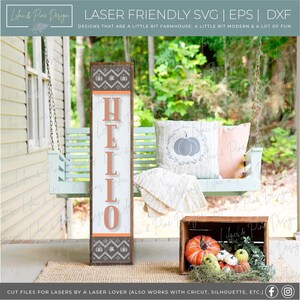 May include: A wooden sign with the word "HELLO" in orange letters on a white background. The sign has a brown border and a patterned design with pumpkins and leaves. The sign is sitting on a porch swing with a pillow that has a wreath and pumpkins on it.