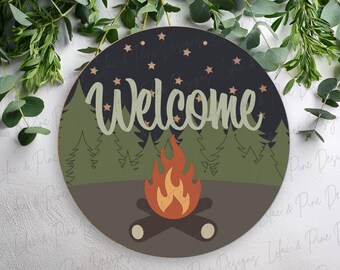 Könnte beinhalten: Runder Holzschild mit Camping-Motiv. Das Schild zeigt das Wort "Welcome" in Schreibschrift, ein Lagerfeuer, Bäume und Sterne. Die Farbpalette umfasst Grüntöne, Braun, Orange und Schwarz.