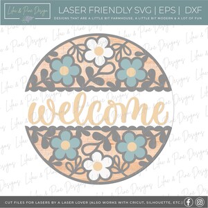 May include: A round wooden sign with a gray border and a floral design in shades of blue, white, and yellow. The sign says "welcome" in a cursive font.