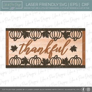 May include: A laser cut design featuring a wooden sign with the word "thankful" in brown script. The sign is decorated with a border of pumpkins and leaves.