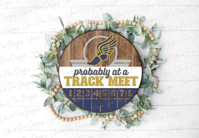 May include: A round wooden sign with a track and field theme. The sign features a winged shoe graphic and the text "probably at a TRACK MEET". The sign is surrounded by greenery and wooden beads.