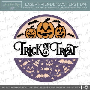 K&ouml;nnte beinhalten: Ein rundes Holzschild mit dem Text "Trick or Treat" in schwarzen Buchstaben. Das Schild ist in zwei H&auml;lften geteilt, wobei die obere H&auml;lfte drei orangefarbene K&uuml;rbisse mit schwarzen Augen, Nasen und M&uuml;ndern zeigt. Die untere H&auml;lfte ist lila und zeigt eine Vielzahl von Halloween-Motiven, darunter Flederm&auml;use, Sterne, Mais und Hexenh&uuml;te.