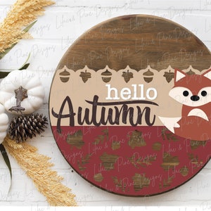 May include: A round wooden sign with a brown and tan background. The sign says "hello autumn" in white letters with a brown fox sitting on the bottom right corner. The sign is decorated with acorns and leaves.