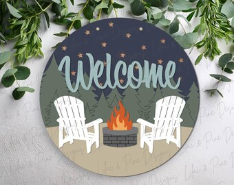 Könnte beinhalten: Runder Holzschild mit Camping-Motiv. Es zeigt das Wort "Welcome" in türkisfarbener Schrift, zwei weiße Adirondack-Stühle, ein Lagerfeuer und eine Waldszene unter einem Sternenhimmel.