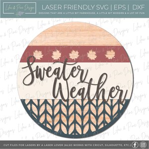 May include: A round wooden sign with the words "Sweater Weather" in a script font. The sign features a cream-colored background with a burgundy stripe and leaf accents. The bottom has a blue knit pattern.