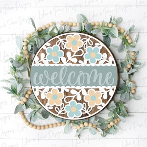 May include: A round wooden sign with a blue and white floral design and the word "welcome" in a light blue script font.
