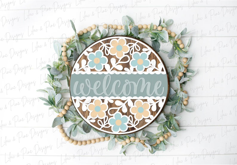 May include: A round wooden sign with a blue and white floral design and the word "welcome" in a light blue script font.