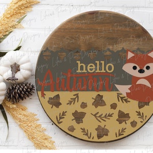 May include: A round wooden sign with a brown woodgrain finish. The sign features a painted fox with a gray face and orange body, surrounded by leaves and the text "hello autumn".