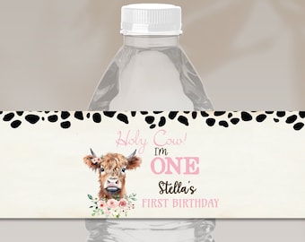 May include: A clear plastic water bottle featuring a rectangular label with a cream background, black cow-print border, and a highland cow illustration. The text reads Holy Cow! I'm ONE Stella's FIRST BIRTHDAY in pink and black lettering.