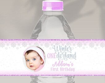 Peut inclure: Une étiquette de bouteille d'eau rose et blanche avec un motif de flocon de neige. L'étiquette indique "Winter Wonderland" et "Addison's First Birthday". Il y a une photo d'une petite fille dans le coin de l'étiquette.