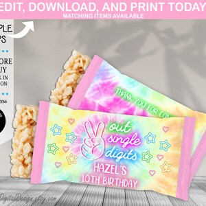 Pode incluir: Embalagens de barras de doces com tema tie-dye com o texto "out single digits" e "HAZEL'S 10TH BIRTHDAY." As embalagens apresentam um sinal de paz e gráficos de estrelas e corações. Uma barra de arroz crocante também é visível.