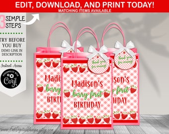 Puede incluir: Bolsas de regalo rosas y blancas con un patrón de fresa y cuadros. Las bolsas tienen un lazo blanco y una etiqueta redonda que dice "¡Gracias por venir!" Las bolsas están decoradas con el texto "Madison's berry first birthday".